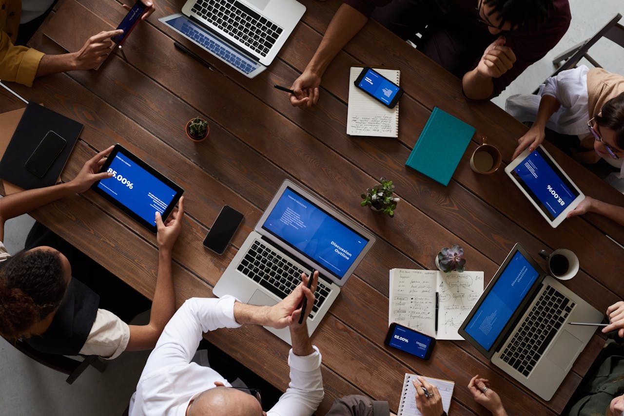 Strona główna Overhead view of a diverse team discussing around a wooden table, using technology.